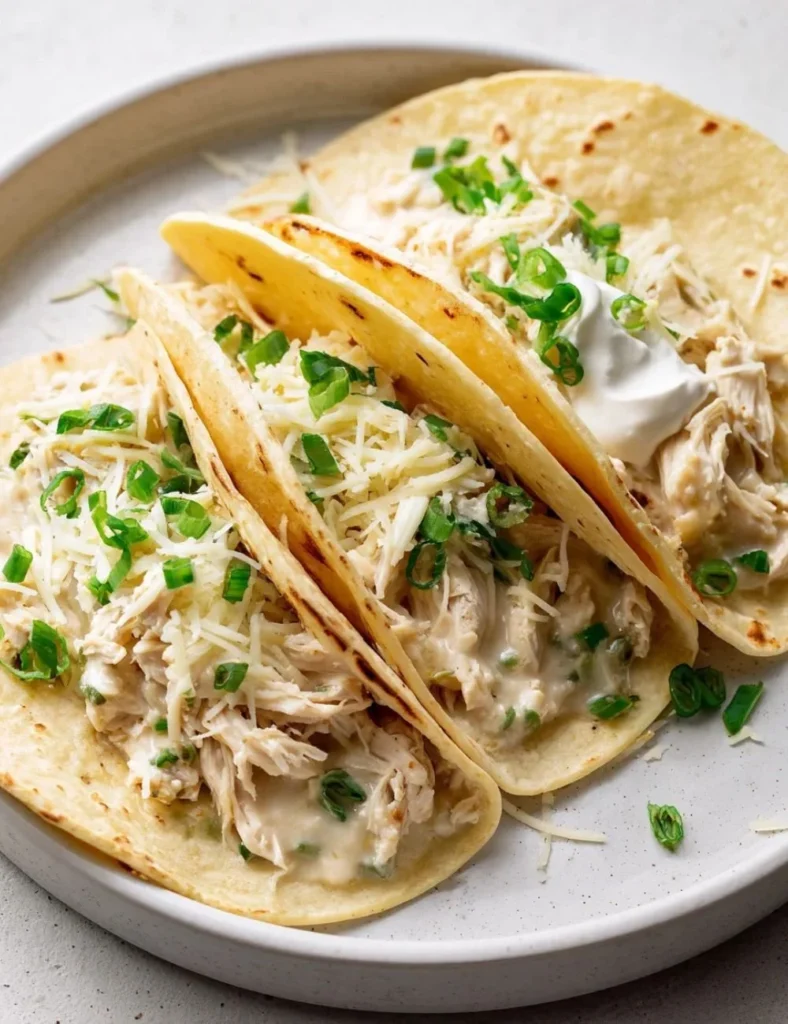 A plate of white chicken chili tacos topped with cilantro and cheese