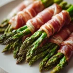 Beef prosciutto wrapped around fresh asparagus spears on a plate.