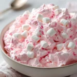 A bowl of Pink Fluff Delight dessert garnished with sprinkles and berries.
